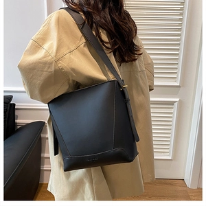 Close-up of minimalist black matte leather tote with debossed corner and wide shoulder strap