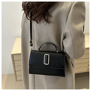 Close-up of minimalist black square handbag with metal clasp and adjustable strap