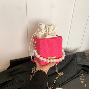 Fuchsia woven bucket bag with pearl handle and chain strap on a black jacket