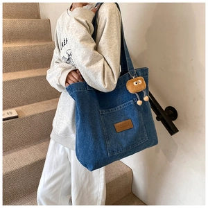 Detail of blue denim tote bag with front pocket and plush monster charm on casual outfit