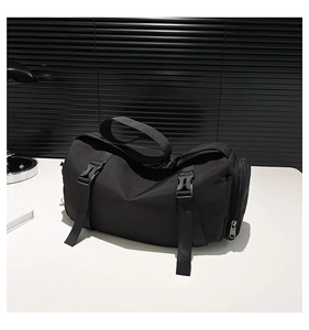Detail of black cylindrical messenger bag with adjustable buckles and side zip pocket