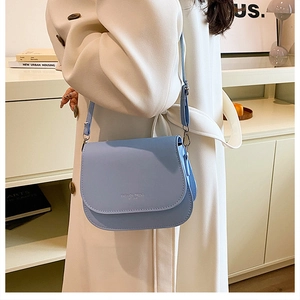 Detail of light blue crossbody bag with fashion trend text and adjustable strap on model