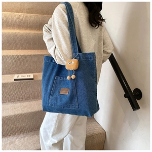 Détail du sac cabas en denim bleu avec étiquette en cuir brun et breloque biscuit