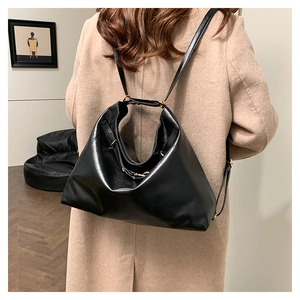 Detail view of large black leather tote bag with gold buckle on a shoulder strap