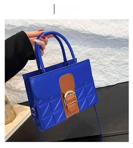 Détail du sac matelassé bleu avec lanières en cuir marron et boucle dorée en forme de D