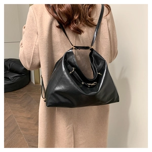Close-up of black leather tote bag with gold metal buckles and slim straps on model