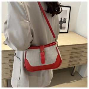 Detailed view of canvas shoulder bag with red leather trim worn by a model in interior