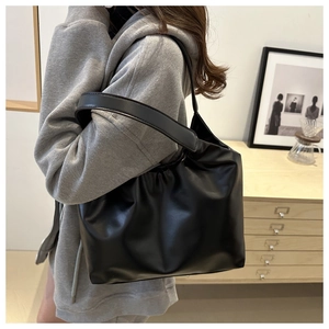 Detail of minimalist black PU leather tote bag with pleated design and wide shoulder strap