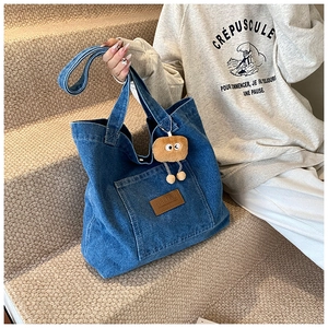 Detail of deep blue denim tote bag with leather logo patch and cute plush charm on strap