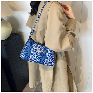 Detailed shot of a blue leopard print hobo bag with gold metal trim on a beige trench coat