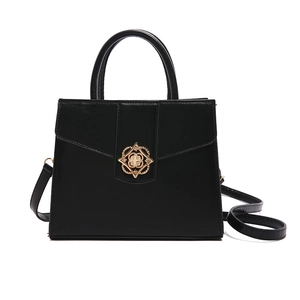 Sac à main noir structuré avec fermoir fleuri doré et bandoulière sur fond blanc uni