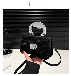 Detail of black pleated square handbag with silver metal handle and detachable strap