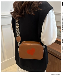Detail of a brown crossbody bag featuring a red heart and geometric patterned strap