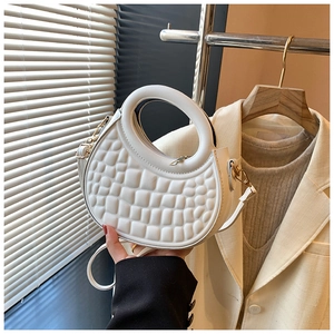 Close-up of a white crescent handbag with embossed texture and round cut-out handle