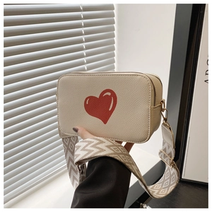 Detail of cream camera bag with red heart print and geometric woven shoulder strap