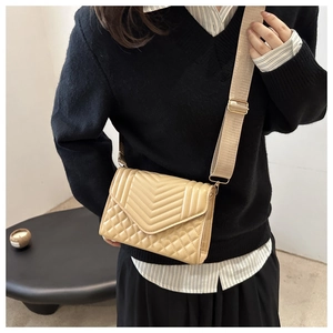 Detail of beige quilted crossbody bag with adjustable wide strap and V-shaped stitching