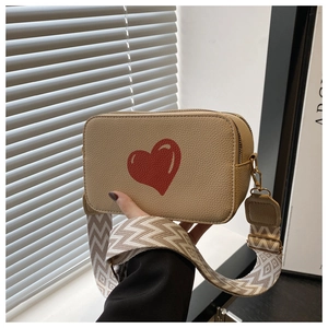 Detail of beige litchi leather camera bag with red heart and patterned wide strap