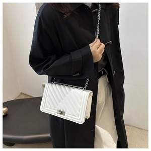 Detail of white quilted crossbody bag with silver chain strap and metal lock closure