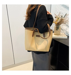 Grand sac cabas beige avec bordure marron porté à l'épaule dans une pièce moderne