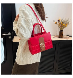 Détail d'un sac porté épaule matelassé rouge avec sangle marron et boucle dorée