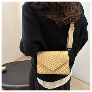 Detail of beige quilted crossbody bag with V-shaped stitching and wide fabric strap