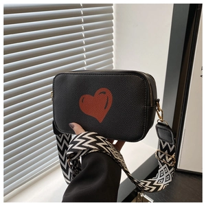 Detail of black pebbled leather crossbody camera bag with red heart print and wide strap