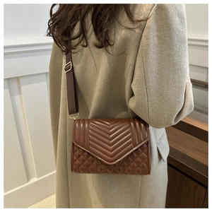 Detailed close-up of brown quilted crossbody bag with V-shaped stitching and wide strap