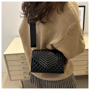 Close-up of black quilted shoulder bag with V-shaped stitching and wide strap on a model
