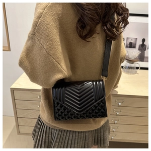 Detail of black quilted crossbody bag with wide strap and gold hardware on model