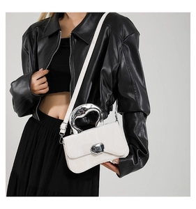 Close-up of white leather handbag featuring unique silver irregular metal handle and heart lock