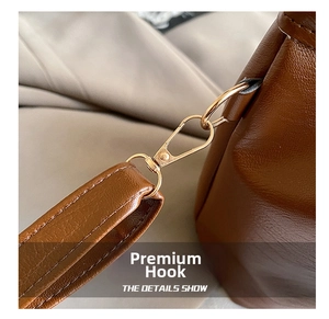 Detail of the golden metal hook and textured leather shoulder strap of the brown bucket bag
