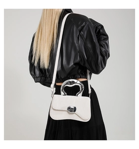 Detail of white patent leather handbag featuring unique silver curved handle on model