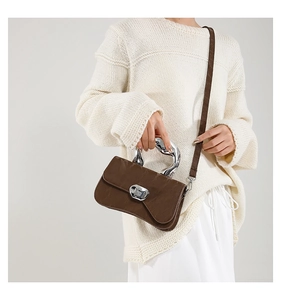 Detail of brown pleated handbag featuring unique silver metal handle and magnetic closure