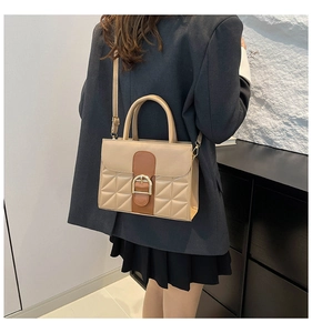 Détail des coutures contrastées beige et marron avec boucle dorée en fer à cheval sur sac