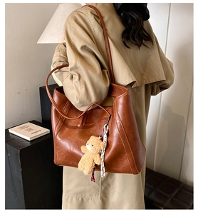 Brown leather tote bag with teddy bear charm shown on model in minimal studio