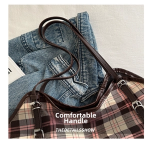Detail shot of the adjustable brown leather strap and silver metal buckle on a plaid tote