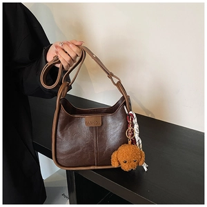 Detail of dark brown leather shoulder bag with plush dog charm and fashion tag