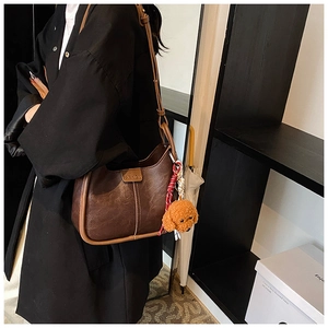 Close-up of retro brown PU leather shoulder bag with fashion embossing and plush charm