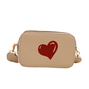Chic beige crossbody bag with red heart pattern and gold hardware on white backdrop