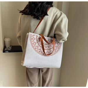 Detail shot of large beige canvas tote bag with brown leather straps worn by a model