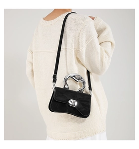 Macro detail of curved black handbag featuring a silver sculptural handle and matte finish
