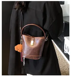 Detail of retro brown bucket bag with textured leather, gold buckle and bear charm