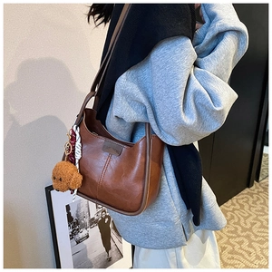 Detail of brown leather hobo bag with teddy bear charm and silk scarf on the strap