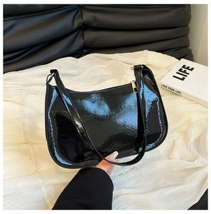 Close-up of black glossy patent leather shoulder bag with golden zipper hardware
