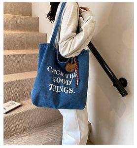Blue denim tote bag with white slogan and brown plush bear charm in a lifestyle setting