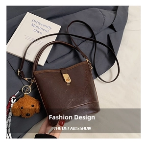Detail view of coffee brown bucket bag with gold hardware and plush teddy charm