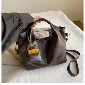 Détail du sac cabas vintage marron avec un mini charm de sac jaune et une chaîne dorée