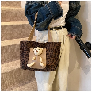 Detail of leopard print tote bag with 3D plush bear and leather handles on shoulder