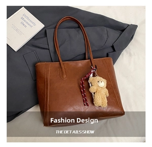 Detail of brown faux leather tote bag with plush bear charm and striped woven rope