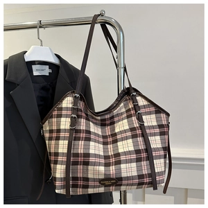 Detail of plaid canvas tote with leather straps and metal brand plate on dark blazer